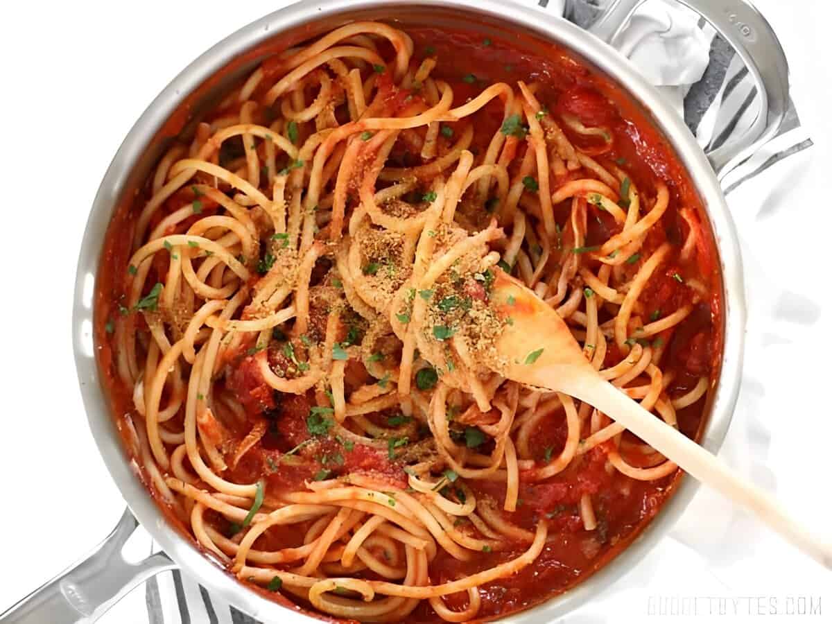 Spaghetti, tomato sauce, toasted breadcrumbs, and herbs in a skillet.