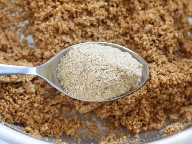 A spoonful of untoasted breadcrumbs held near the skillet of toasted breadcrumbs to show the color difference