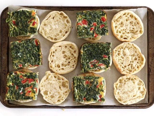 Vegetable egg patties added to english muffins on a baking sheet