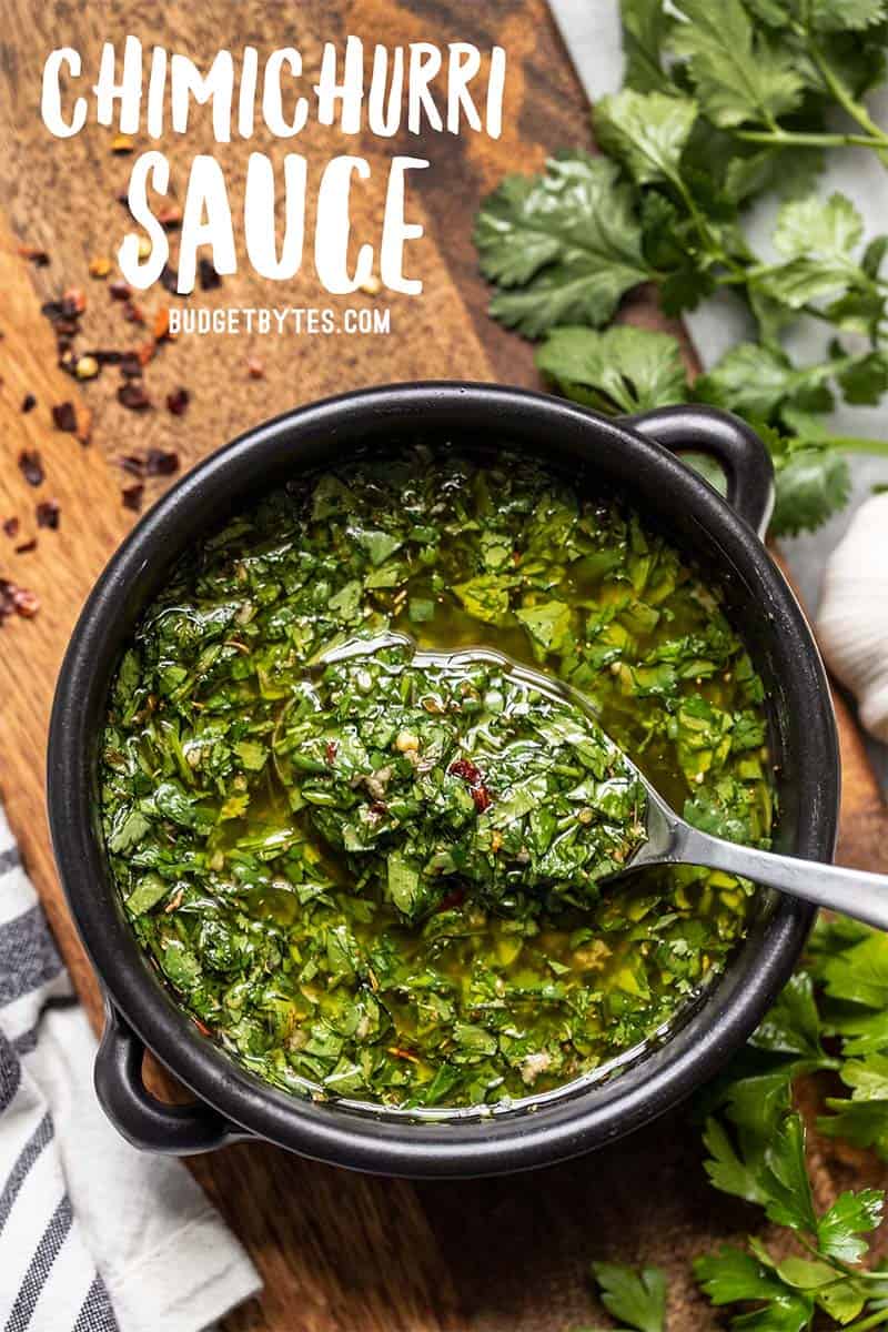 A black bowl full of chimichurri sauce with a spoon lifting some out, close up.