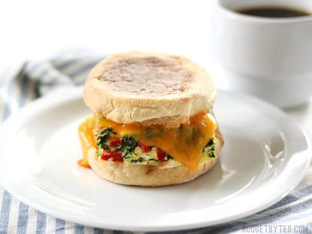 A Veggie Packed Freezer Breakfast Sandwich on a plate with a cup of coffee in the background