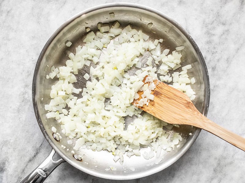 Sautéed onion and garlic in a skillet with a wooden spatula