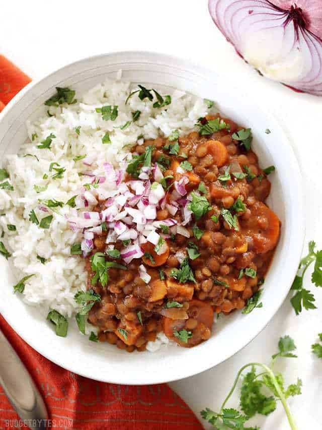 A bowl of Slow Cooker Coconut Curry Lentils garnished with red onion and cilantro