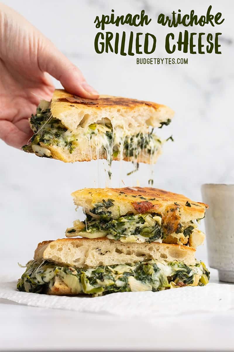 A hand lifting one piece of a spinach artichoke grilled cheese, title text at the top.
