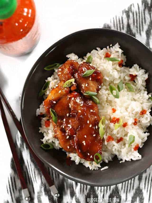 Sticky Ginger Soy Glazed Chicken in a bowl with jasmine rice and garnished with green onion and sriracha