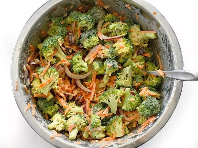 Broccoli salad mixed with the honey yogurt dressing, in the metal mixing bowl