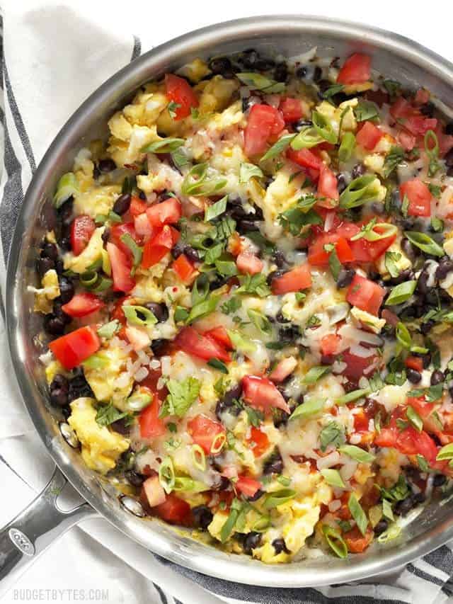 Overhead view of a skillet full of Ultimate Southwest Scrambled Eggs topped with tomato and green onion
