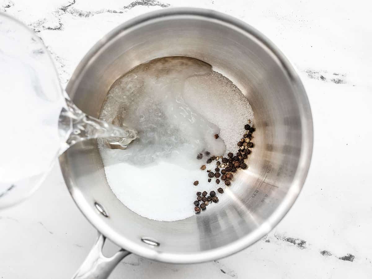 Salt, sugar, and peppercorns in a saucepot, vinegar being poured over top