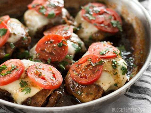 Side view of balsamic chicken in the skillet with melty mozzarella and tomato slices on top