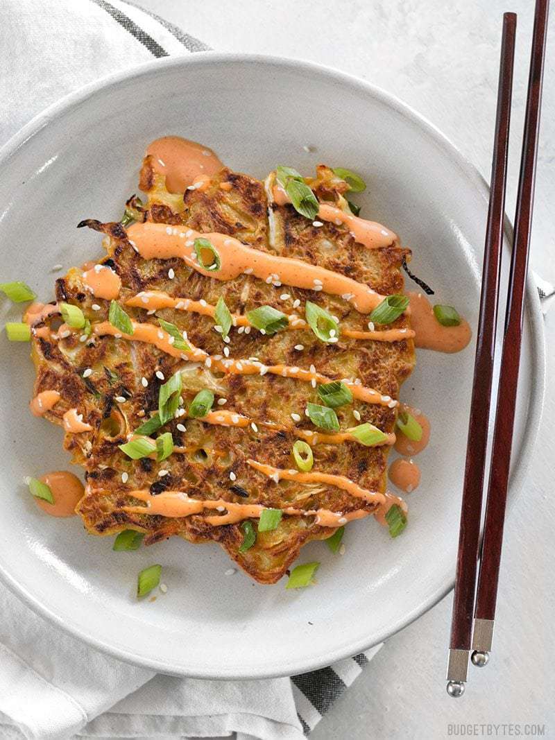 One savory cabbage pancake on a plate with sriracha mayo and chopsticks on the side.