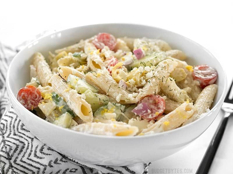 Side view of Creamy Lemon Dill Greek Pasta Salad in a bowl on a striped napkin with a black fork on the side