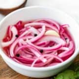 Side view of a bowl of pickled red onions on a wooden plate