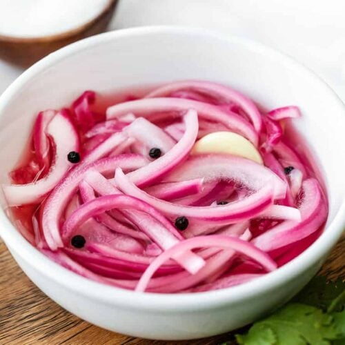 Side view of a bowl of pickled red onions on a wooden plate