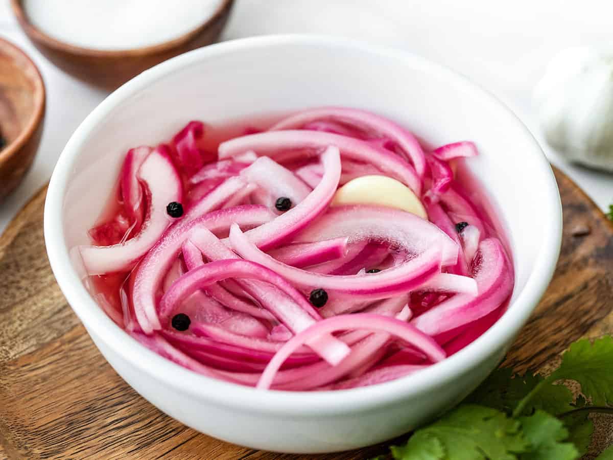 Side view of a bowl of pickled red onions on a wooden plate