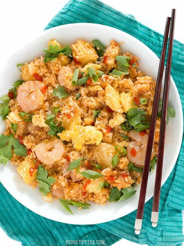 Overhead view of a large bowl full of Shrimp Fried Rice with Pineapple and Toasted Coconut on a teal napkin with wooden chopsticks