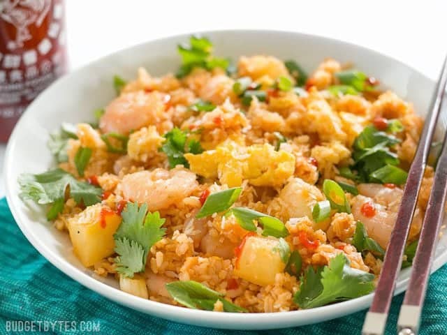 Front view of a bowl of Shrimp Fried Rice with Pineapple and Toasted Coconut with a bottle of sriracha in the back.