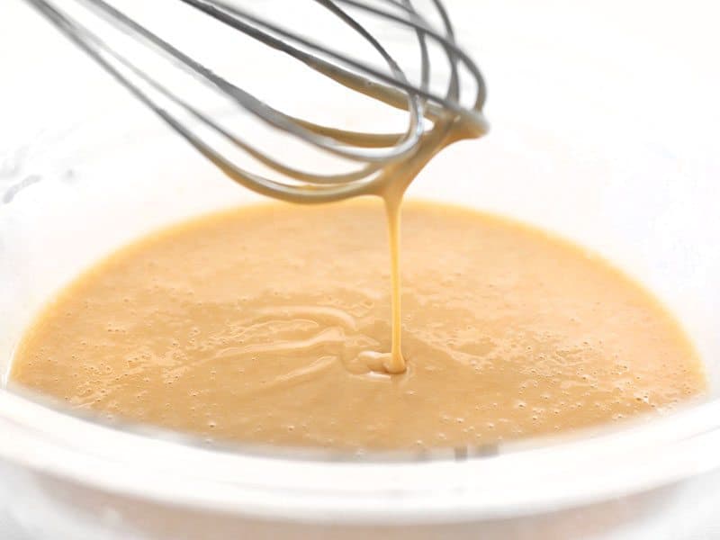 cabbage pancake batter whisked in a bowl, dripping off whisk to show viscosity