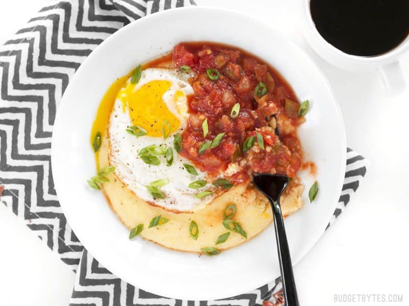 Cheddar Grits Breakfast Bowls are an easy, comforting, and indulgent breakfast or brunch treat that you can whip up in about 30 minutes. BudgetBytes.com Overhead shot of a Cheddar Grits Breakfast Bowl with a fork stuck into the side