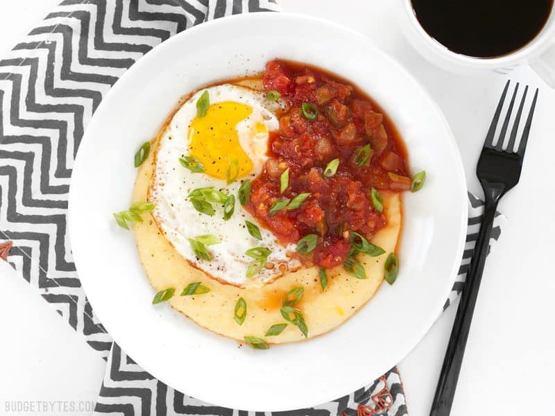 Overhead shot of a Cheddar Grits Breakfast Bowl on a striped napkin with coffee nearby 