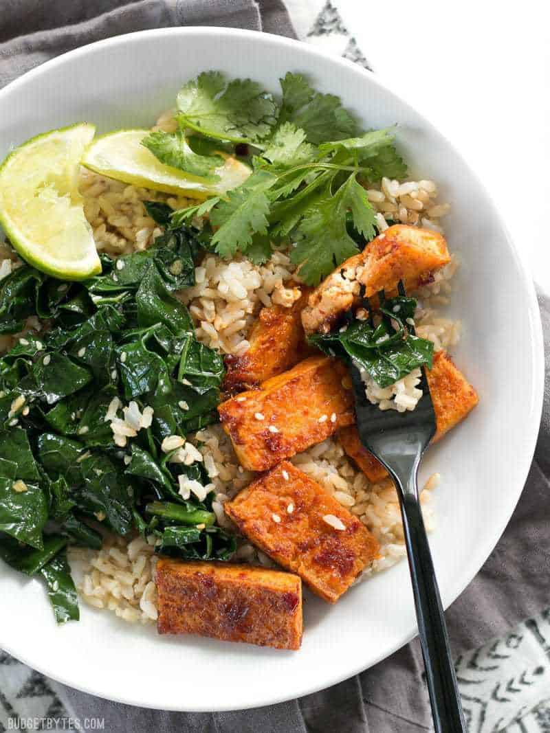 Close up of Chili Garlic Tofu Bowls with a fork piercing a piece of tofu and some kale.