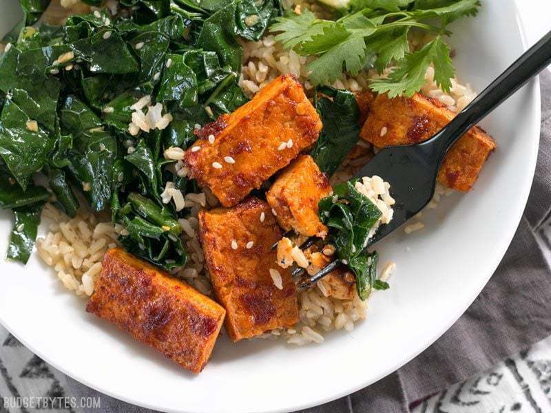 Close up of the bottom half of a Chili Garlic Tofu Bowl with a fork piercing a piece of tofu.