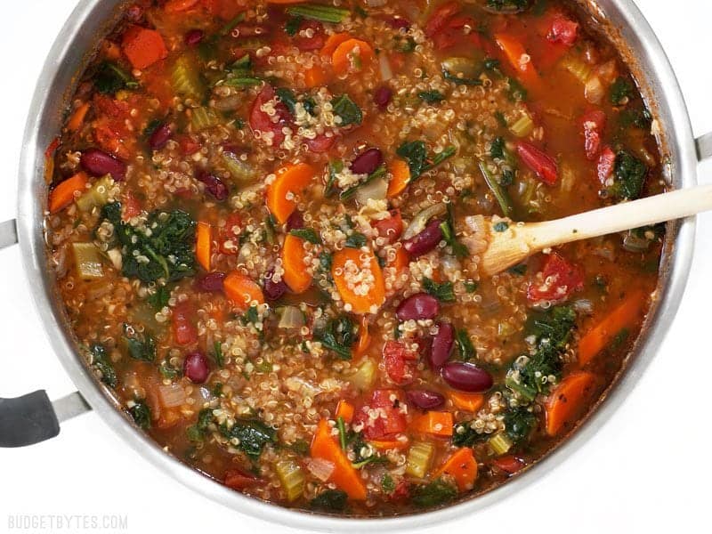 Close up overhead view of the pot full of Garden Vegetable Quinoa Soup with a wooden spoon
