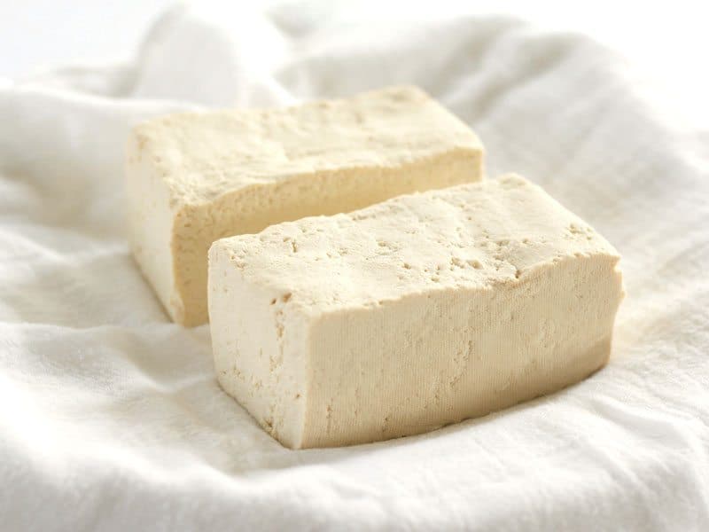 Pressed Tofu block cut into two, sitting on a towel