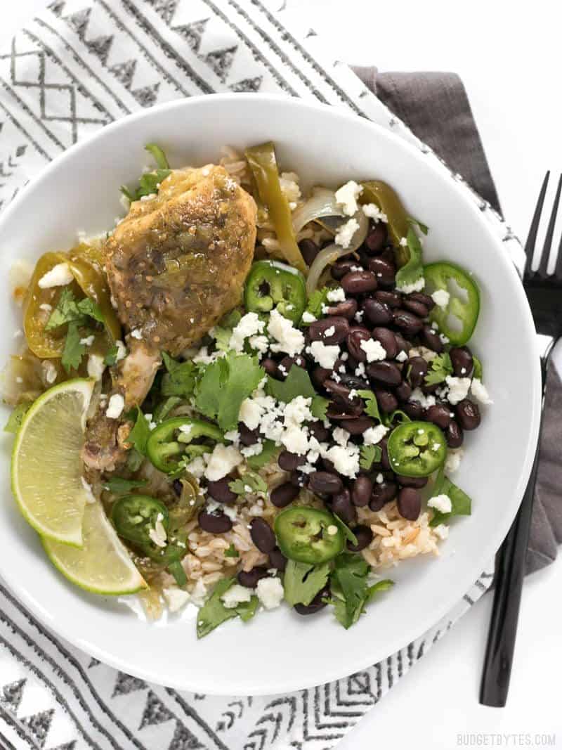 Overhead view of a Slow Cooker Salsa Verde Chicken bowl with rice, beans, jalapeño, cheese, and lime.