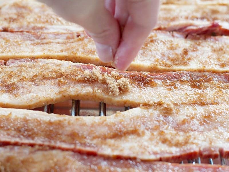 Close up of Brown Sugar being sprinkled on raw thick cut bacon strips