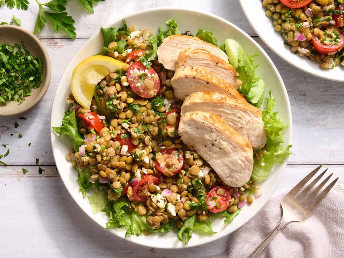 Overhead view of a bowl of marinated lentil salad and grilled chicken.