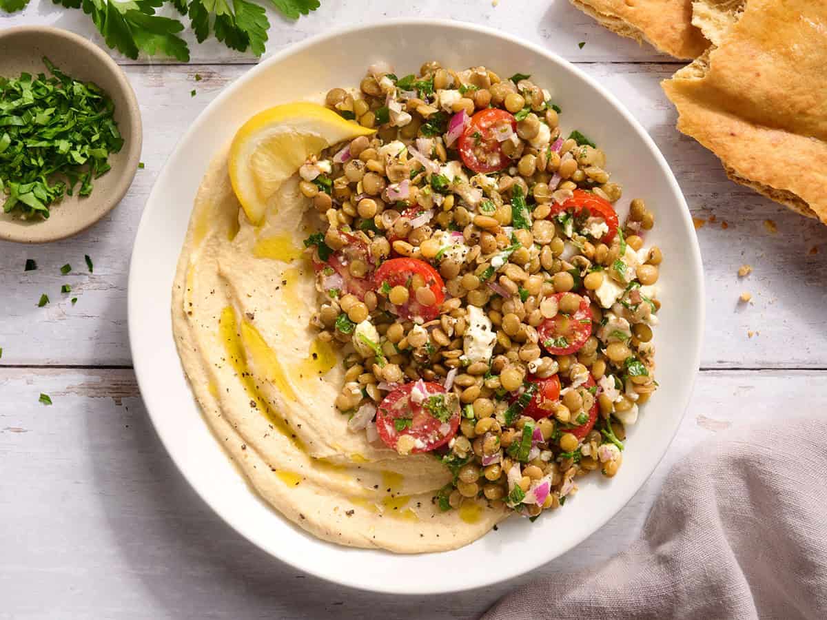 A hummus bowl with lentil salad and a lemon wedge.