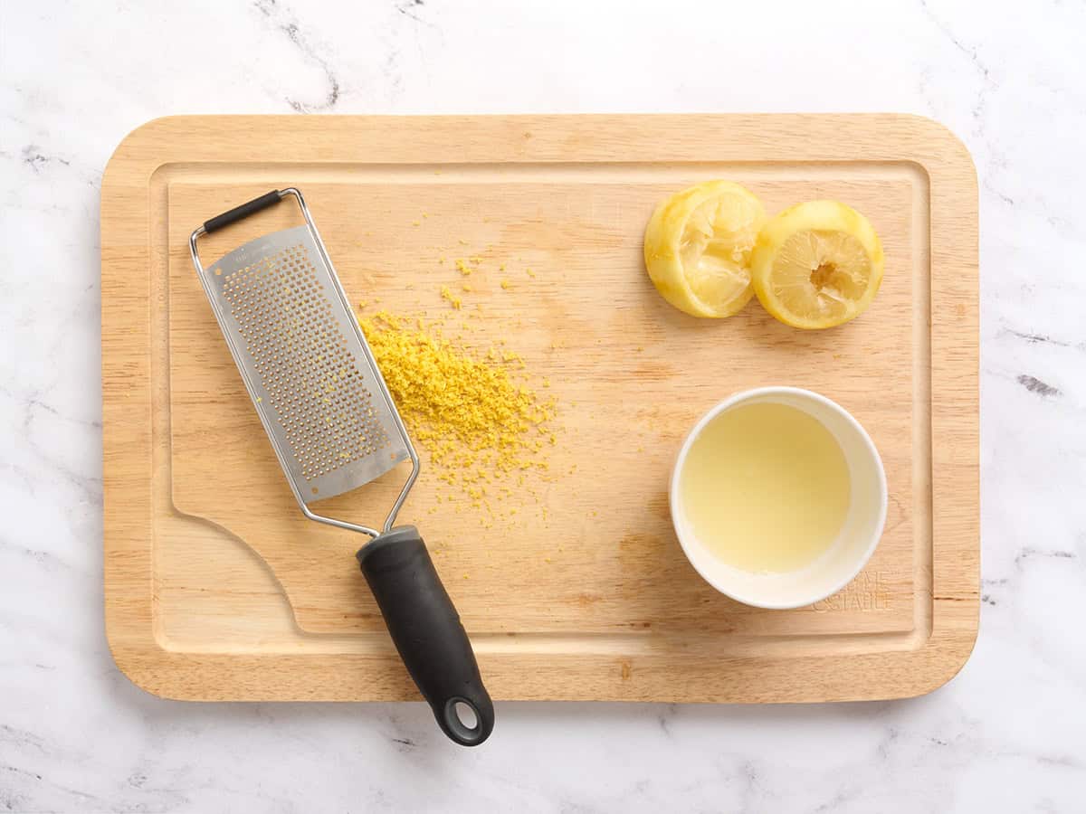 Lemon juiced and zested on a wooden cutting board.