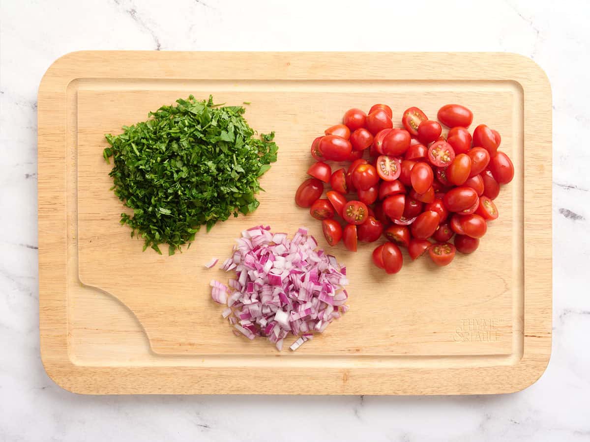 Chopped tomatoes, parsley and redd onion on a cutting board.