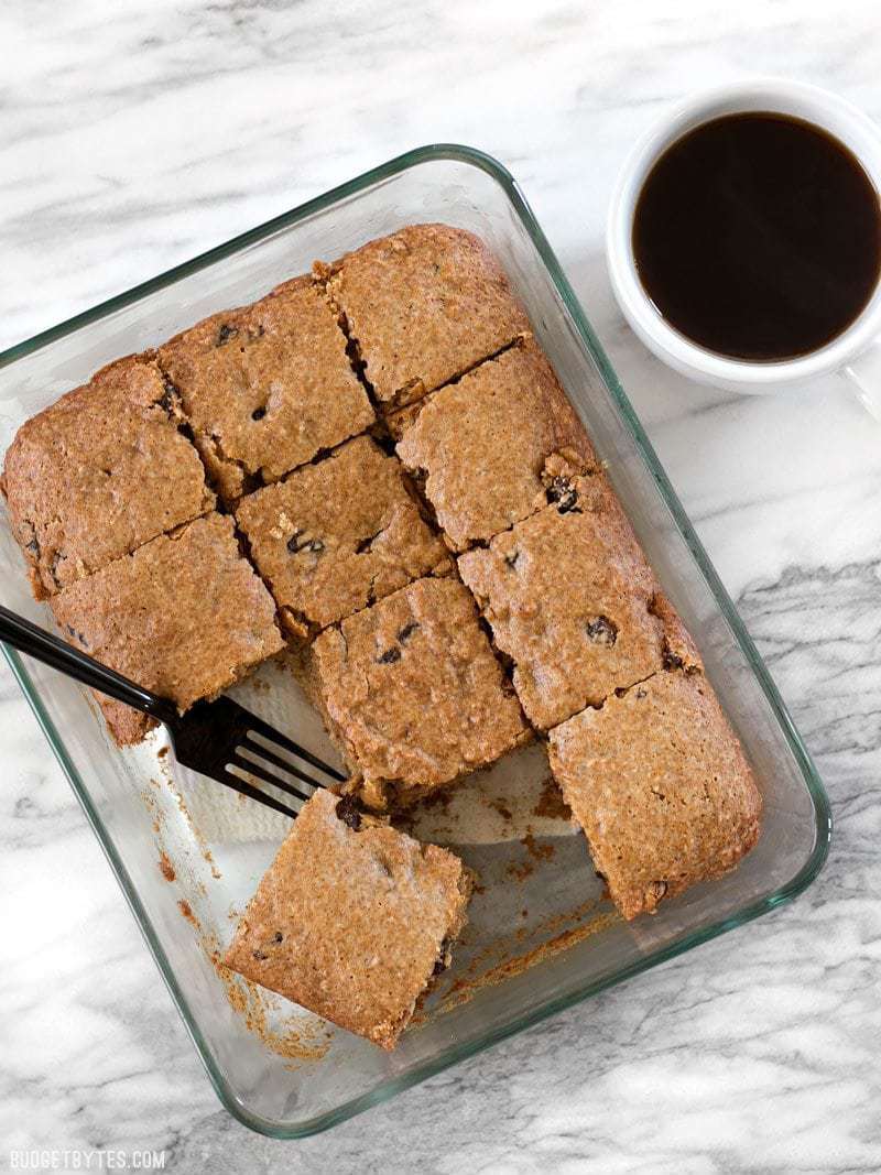 A class casserole dish with baked Applesauce Cake, a fork resting in the dish, a cup of coffee on the side.