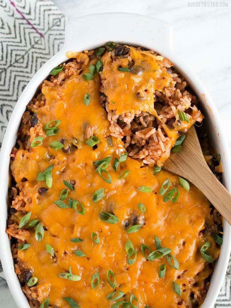Beef Burrito Casserole in an oval white casserole dish being scooped out with a wooden spoon.