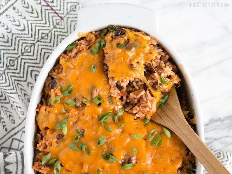 Overhead view of the Beef Burrito Casserole in a casserole dish, being scooped out with a wooden spoon.