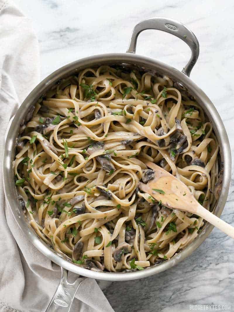 This rich and Creamy Mushroom Herb Pasta is a surprisingly fast and simple to way to have a gourmet meal at home. BudgetBytes.com A skillet full of Creamy Mushroom Herb Pasta garnished with parsley and a wooden pasta fork in the side.