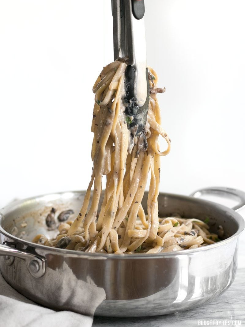 Tongs lifting a bunch of Creamy Mushroom Herb Pasta out of the skillet, viewed from the side.