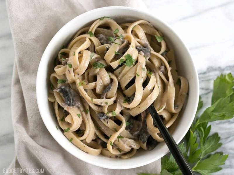 Overhead of Creamy Mushroom Herb Pasta in a bowl with the pasta twirled around a black fork, parsley on the side