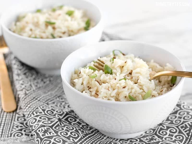 Two bowls of cumin rice, garnished with green onion, and two gold forks. 