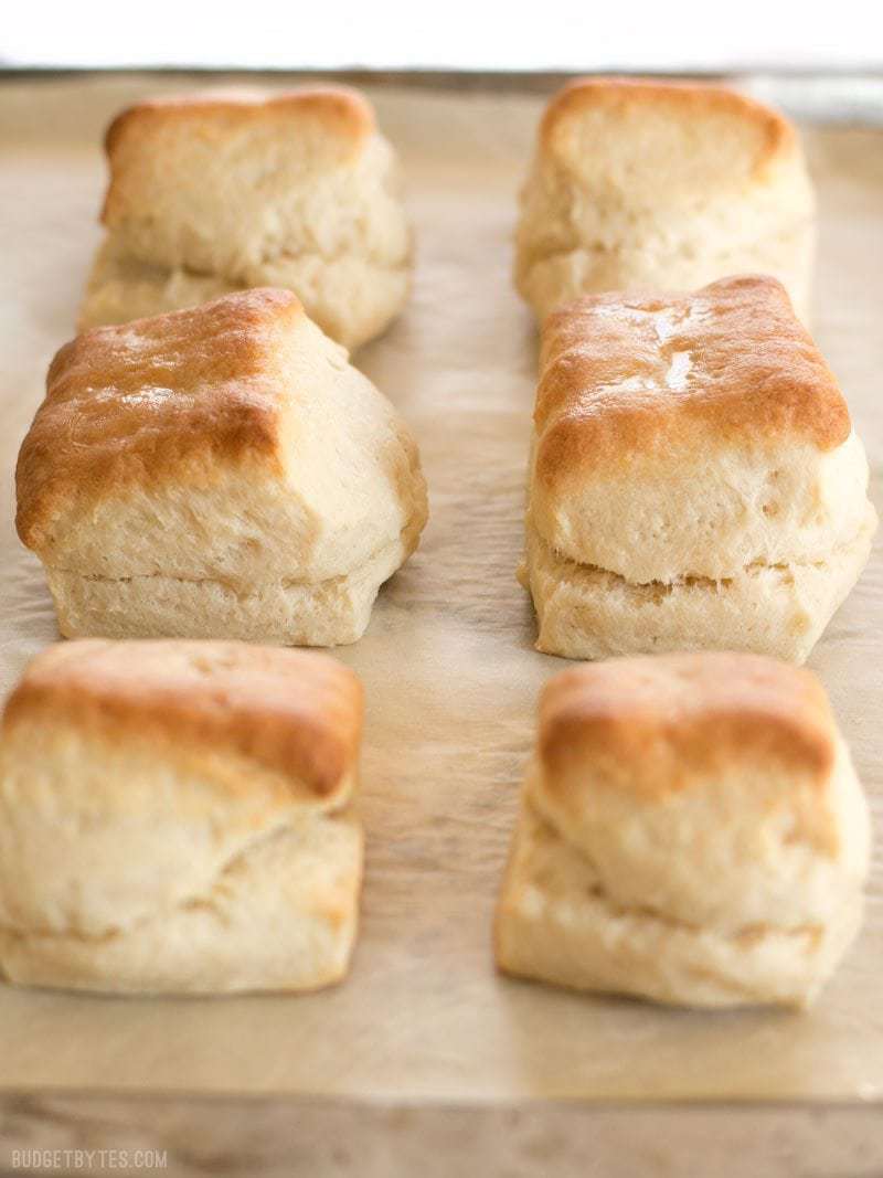 Six Freezer Biscuits perfectly browned and brushed with butter on a parchment lined baking sheet