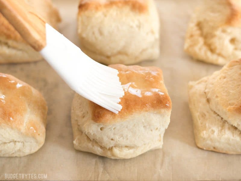 Melted butter being brushed onto a freshly baked Freezer Biscuit with a silicone brush