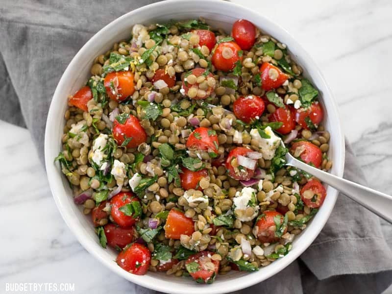 Finished Marinated Lentil Salad in a white bowl, on a grey napkin, with a fork stuck in the side