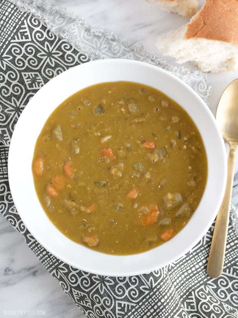 A bowl of Pressure Cooker Split Pea Soup with a gold fork and piece of bread on the side.