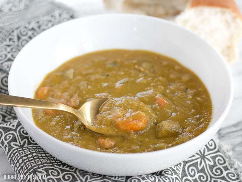 Front view of a bowl of Pressure Cooker Split Pea Soup with a gold spoon lifting a bite.