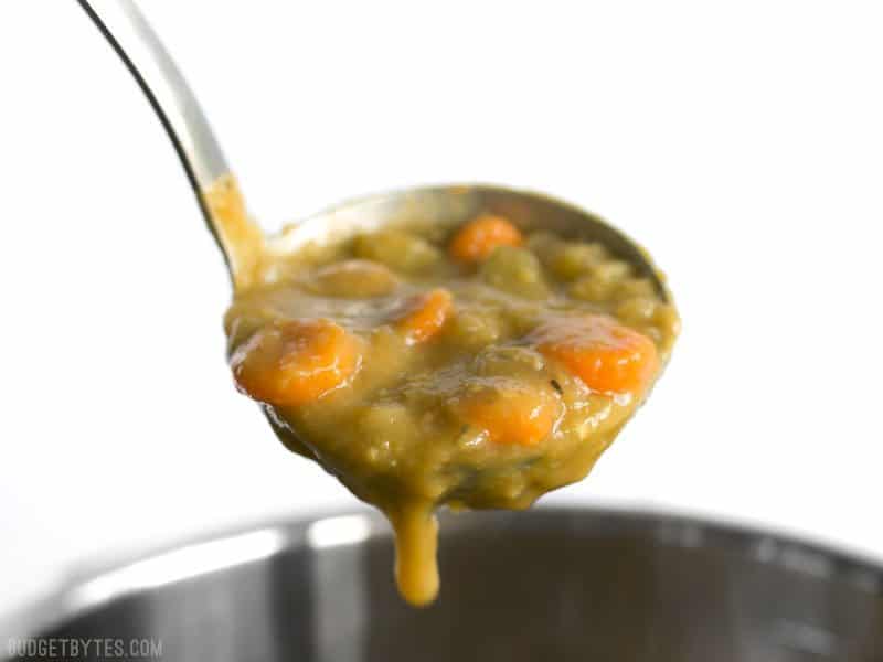 A ladle full of Pressure Cooker Split Pea Soup dripping into the pot.