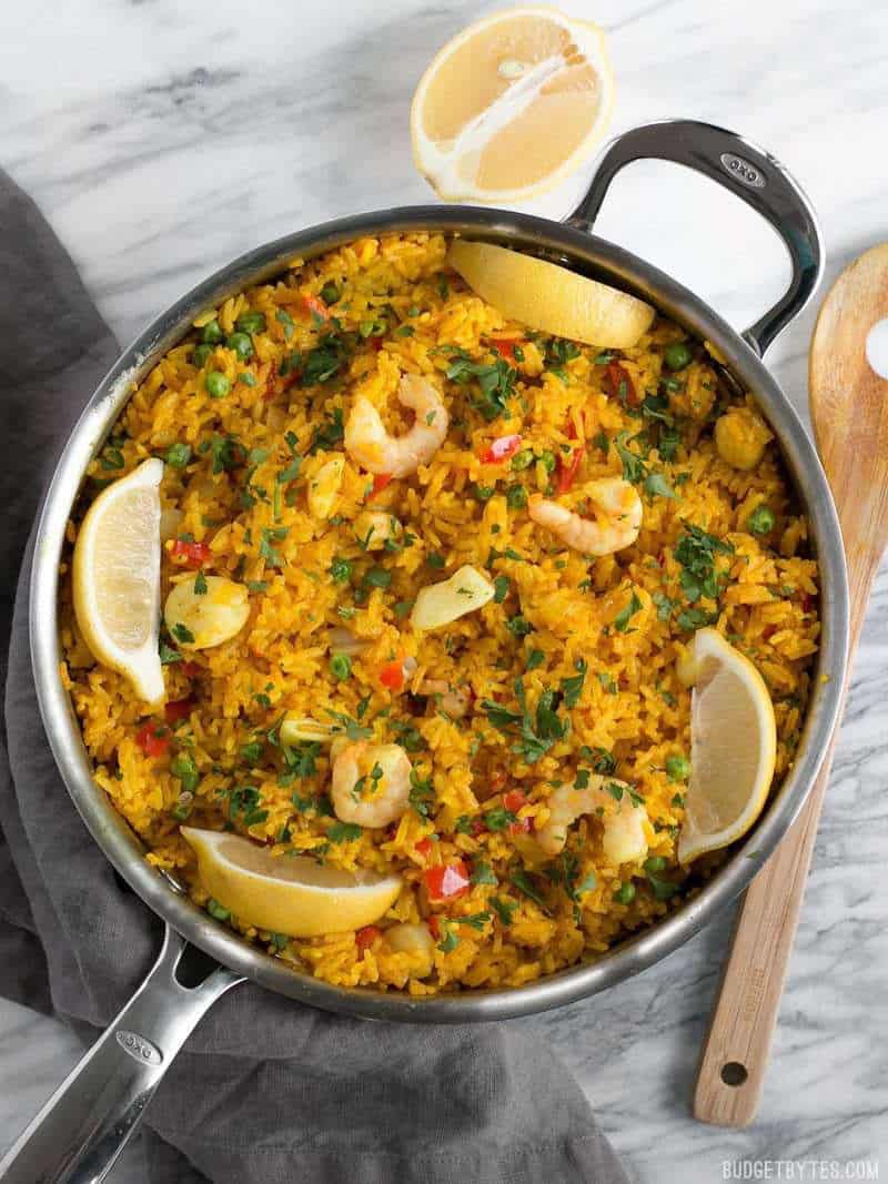 Seafood Rice Skillet garnished with lemon wedges and parsley, viewed from above with a wooden spoon on the side.