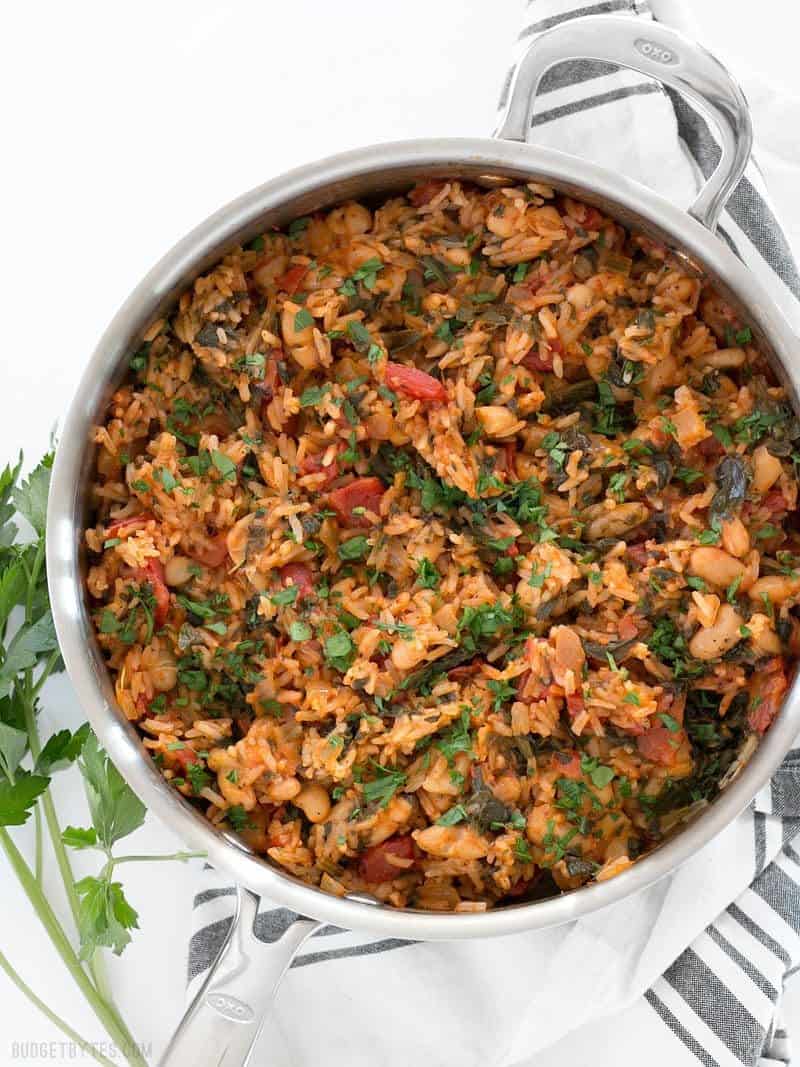 A deep skillet full of Tomato Herb Rice with White Beans and Spinach, garnished with chopped parsley