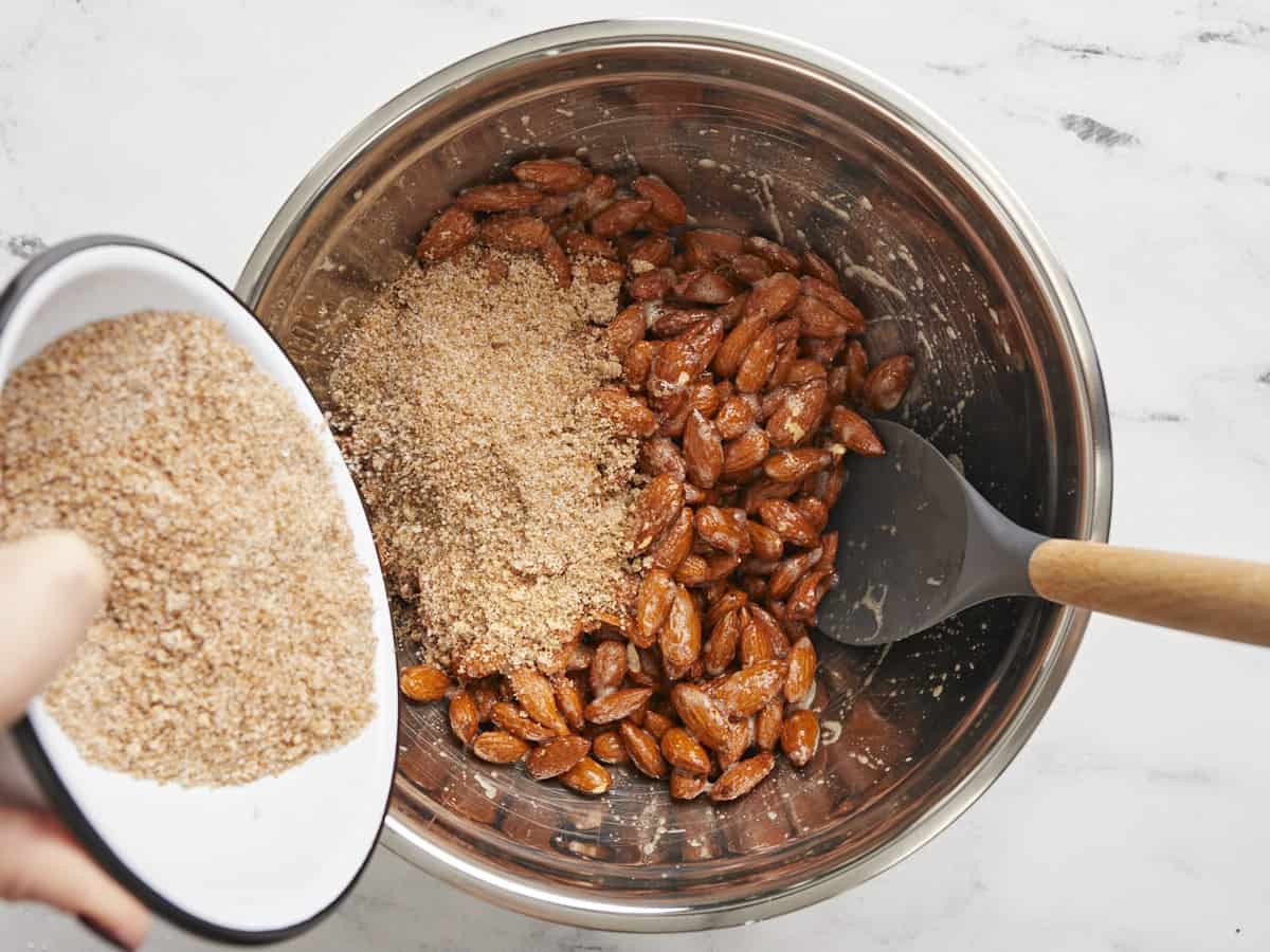 Almonds coated in egg white with sugar mixture being poured into the bowl. 