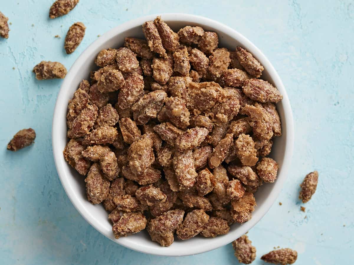 Overhead view of candied almonds in a bowl on a blue background. 